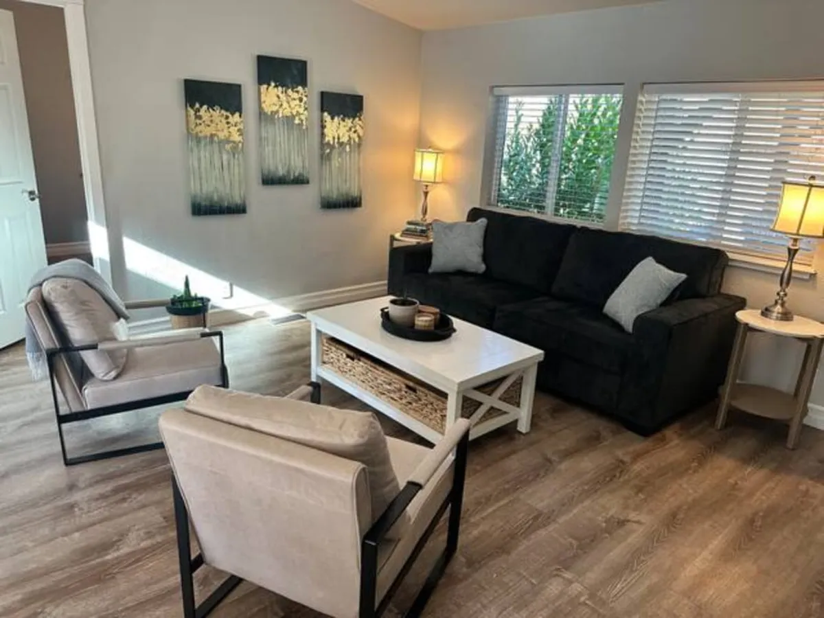 A comfortable living room with a sleek black sofa, curated wall art, a coffee table, and soft lighting from lamps. The setup invites relaxation, conversation, and cozy family evenings, reinforcing the farmhouse's warm atmosphere.
