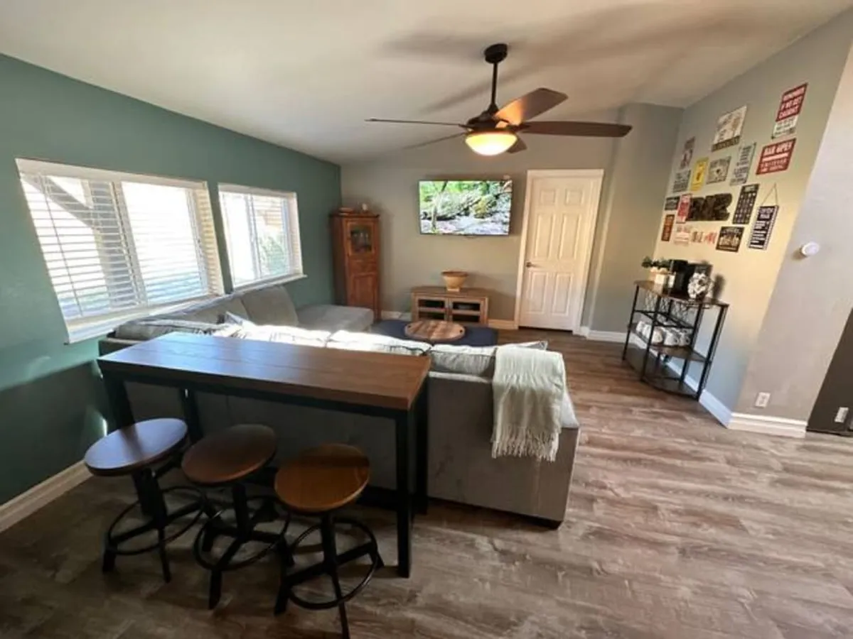 This image includes a sofa, TV, dining table, and decorative wall signs that nod to a heritage aesthetic. The space feels inviting and is decorated to create a lived-in, nostalgic atmosphere, pairing vintage decor with updated comforts.
