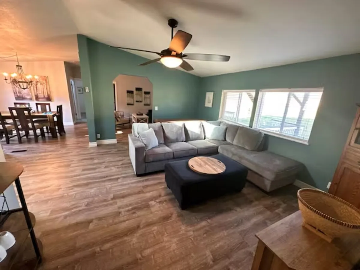 A spacious, inviting open-plan living area that seamlessly combines a large sectional sofa, a round coffee table, and a rustic dining table illuminated by a chandelier. The gathering space is styled for comfort and conversation, ideal for family nights or entertaining guests.