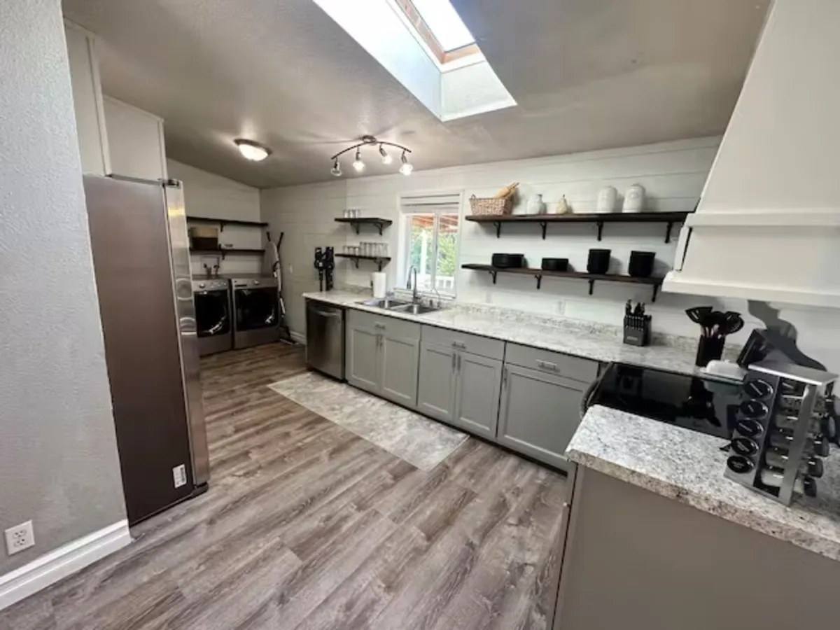A bright, thoughtfully updated kitchen featuring a central island, open shelving with dishware, and modern appliances. Natural light streams in through the windows, emphasizing the kitchen's welcoming mood and readiness for shared meals and conversations.
